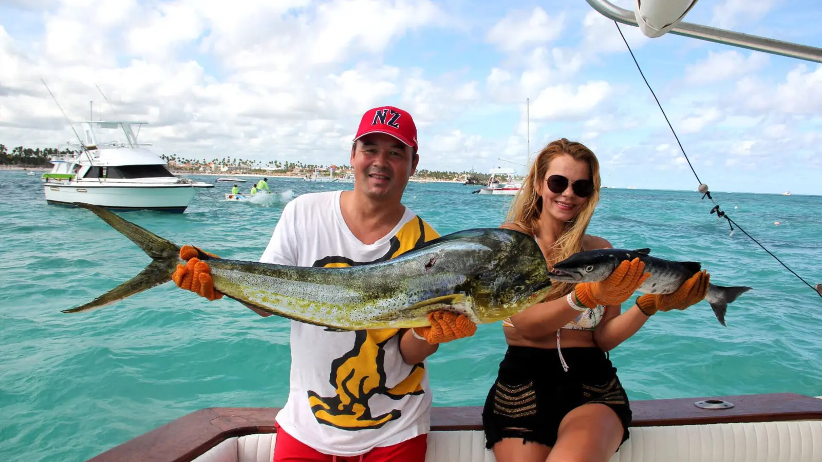 A man and a woman holding a big mahi mahi together, another fishing boat behind