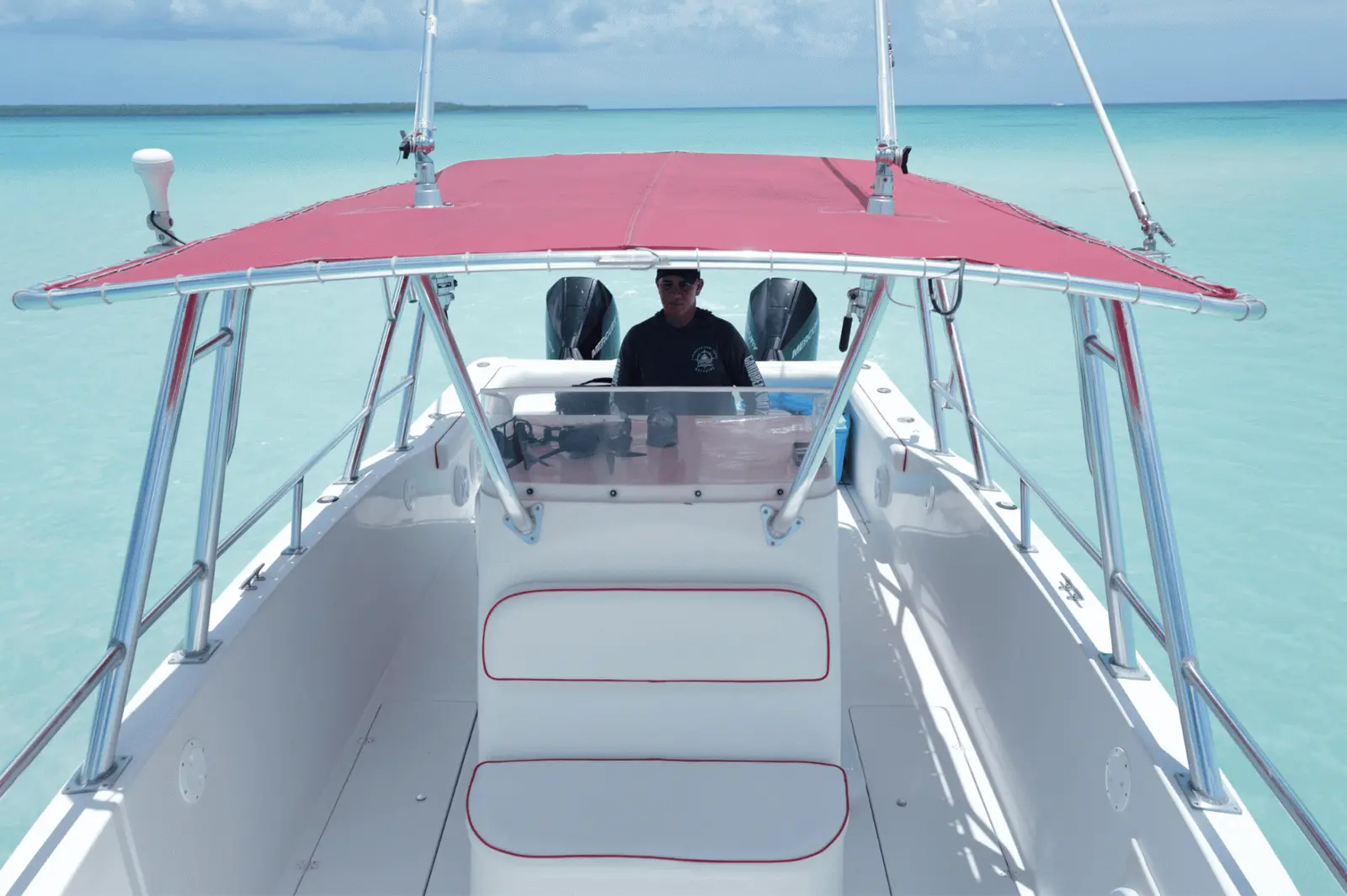 Captain at the console under the red canopy of a speedboat, seen from the bow over clear water