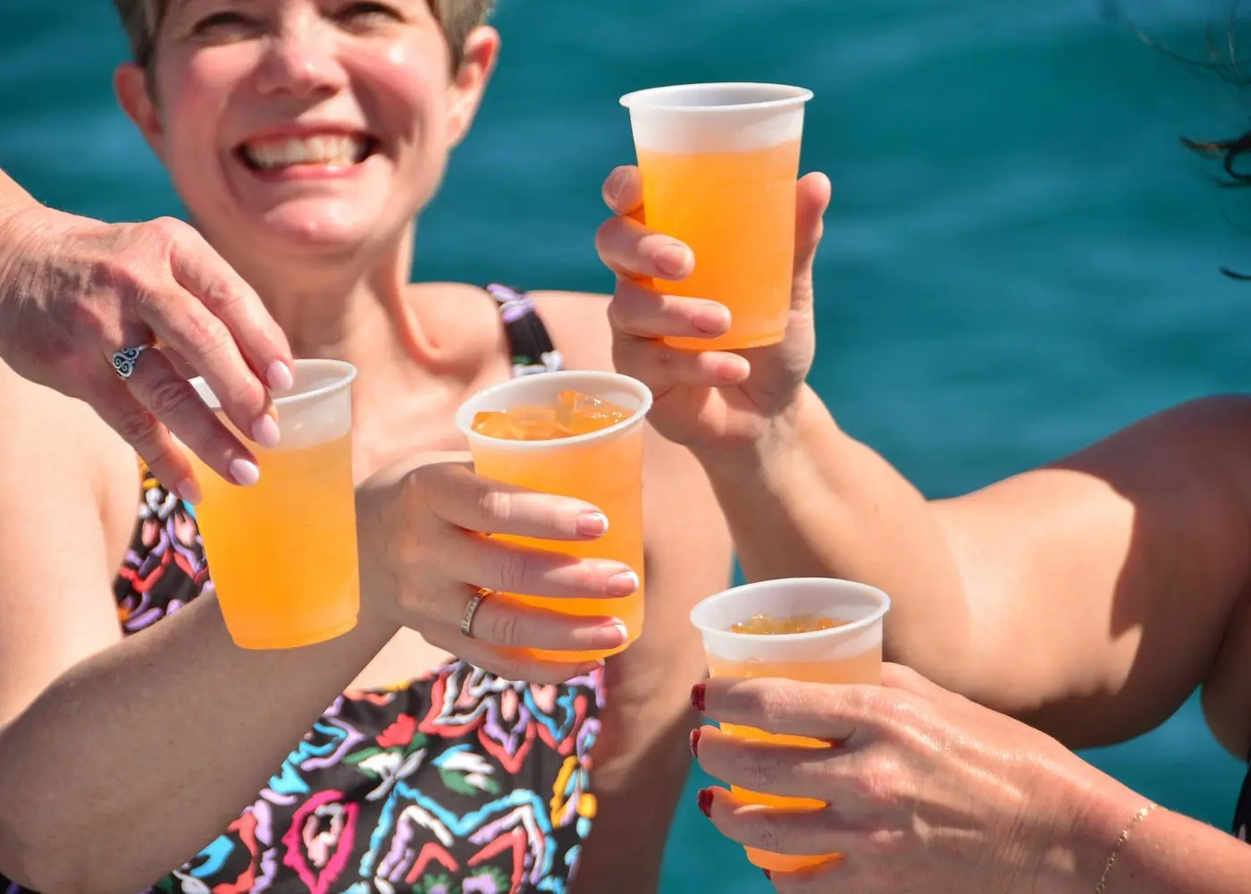 Smiling woman and other guests clinking plastic cups of orange punch by the sea