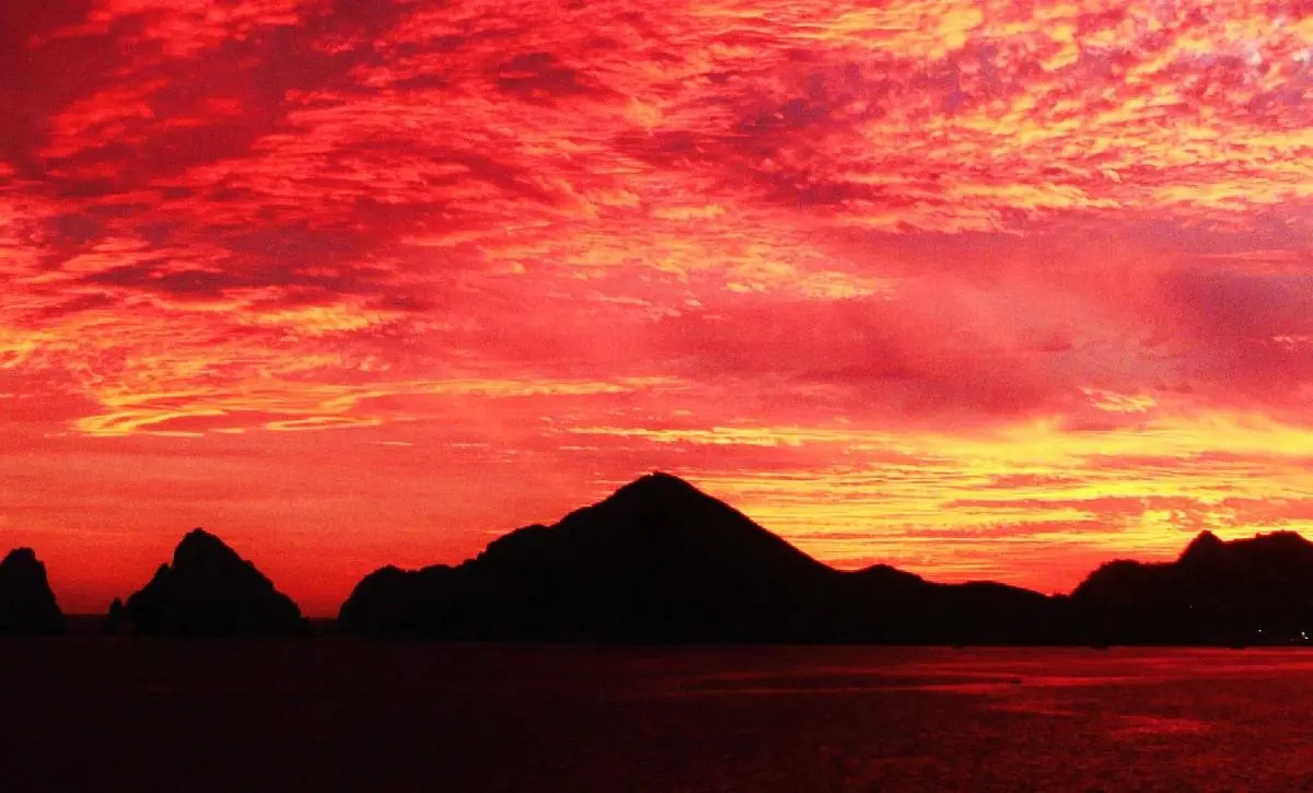 Fiery red and orange sunset sky above the dark silhouetted hills of Cabo San Lucas