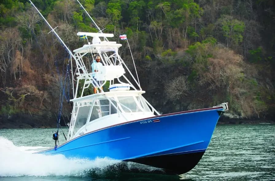 Blue-hulled sportfishing boat with a tall tower running fast along a forested Papagayo shoreline