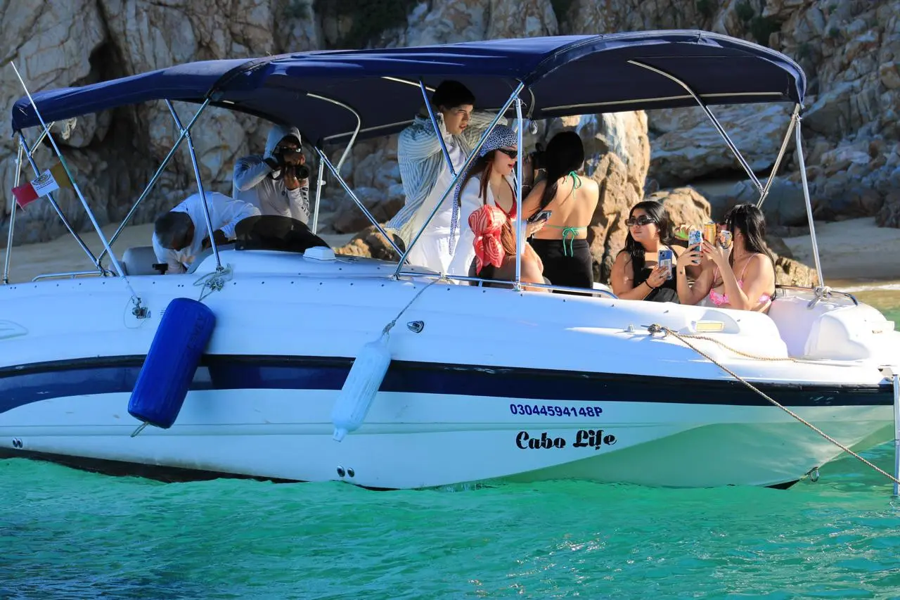 Guests snap photos aboard the canopied small yacht anchored in turquoise water off Cabo San Lucas
