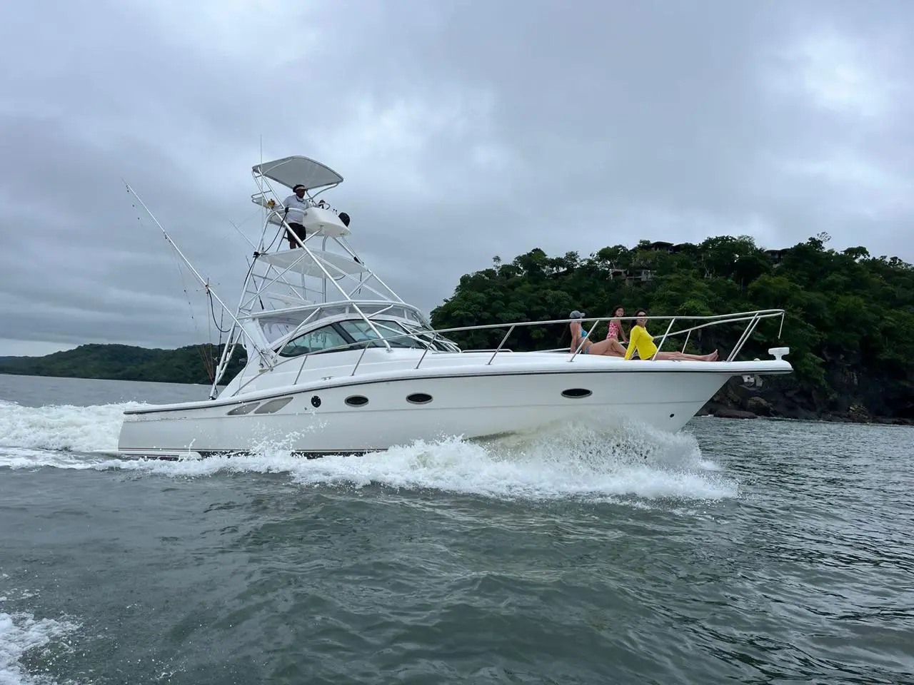Sportfishing yacht with a tuna tower cruising past a forested headland in Costa Rica, guests on the bow