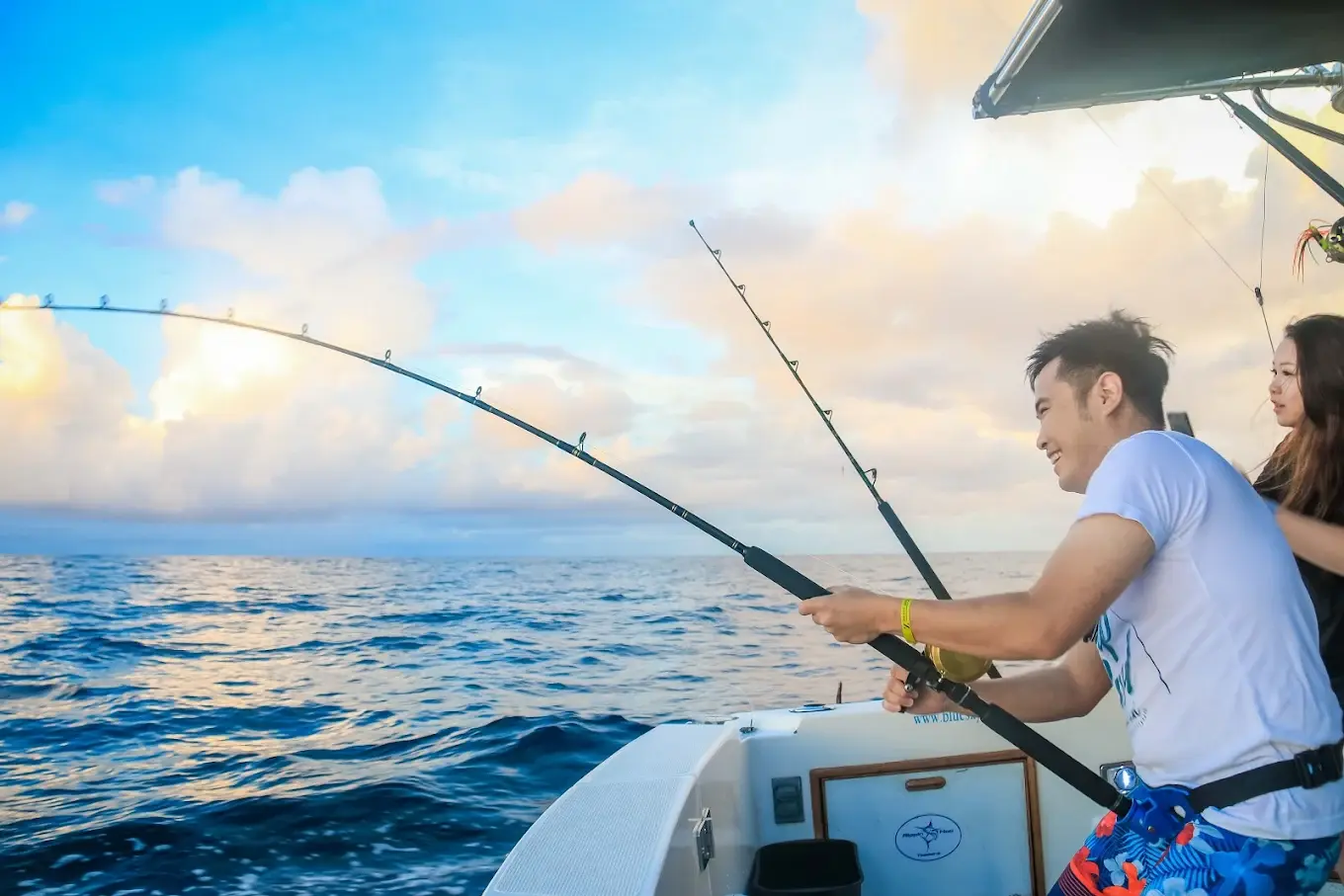 Angler in a fighting belt reeling in a fish on a bent rod from the cockpit at golden hour
