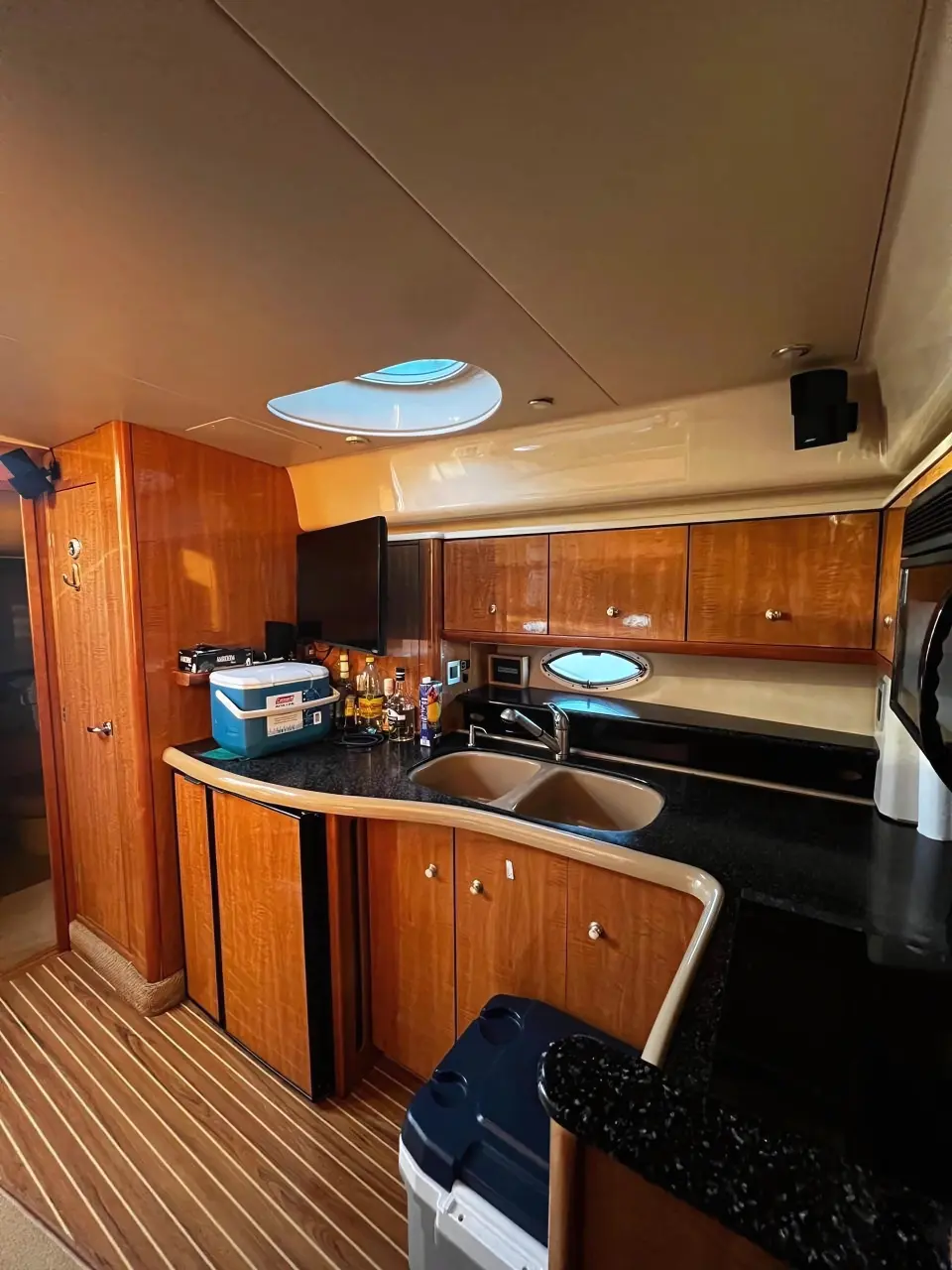 Yacht galley below deck with a double sink, wood cabinetry, an overhead hatch and a cooler