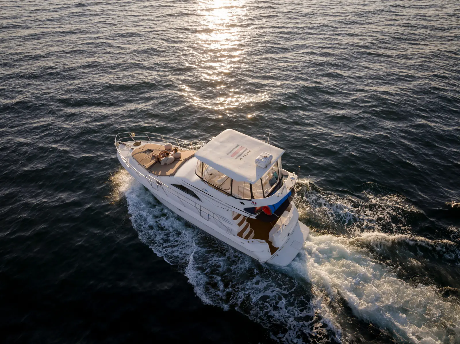 Aerial view of a flybridge motor yacht cutting a wake across sunlit water in the Gulf of Papagayo