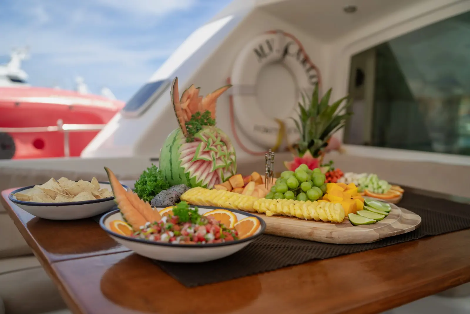 Fruit platter, fresh salsa and tortilla chips set out on a teak table aboard a catamaran