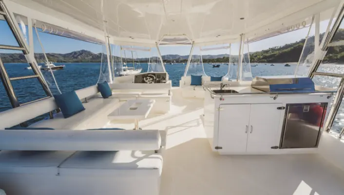 Shaded flybridge of a power catamaran with lounge seating and a wet bar overlooking a green Costa Rica bay