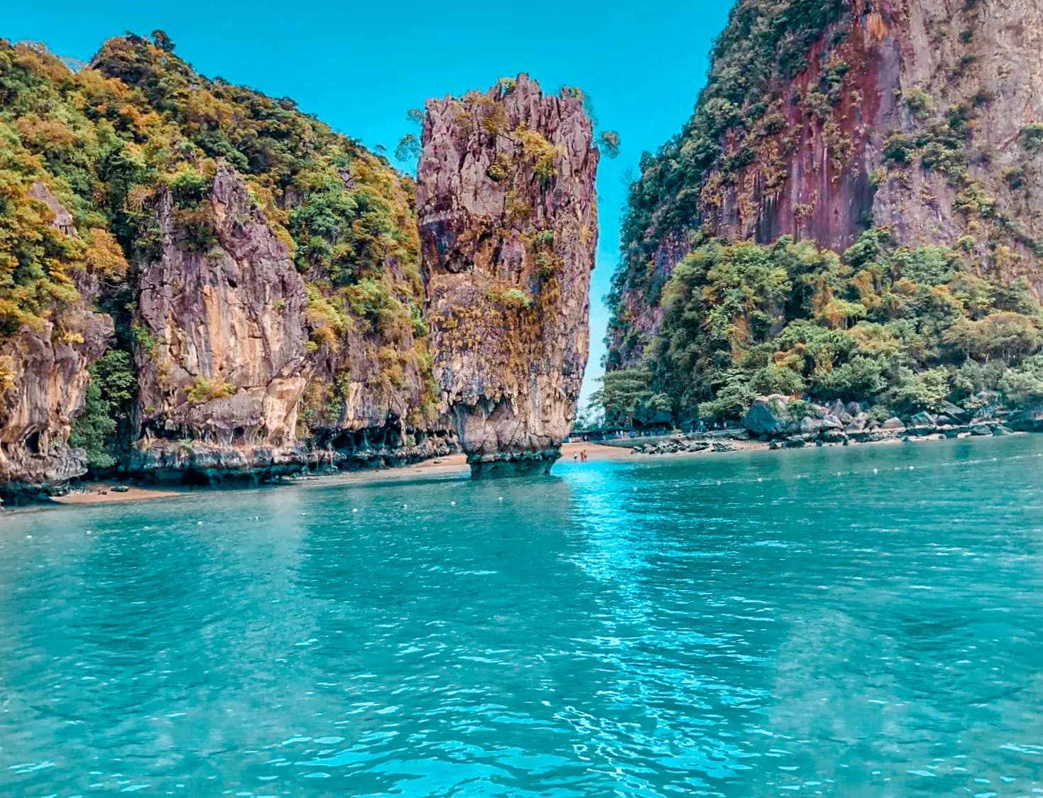 Slender limestone sea stack rising from turquoise water between karst cliffs in Phang Nga Bay