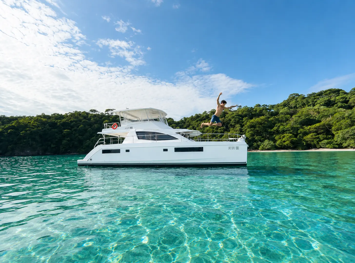 A guest leaps off the top deck of a power catamaran anchored in clear turquoise water off Costa Rica