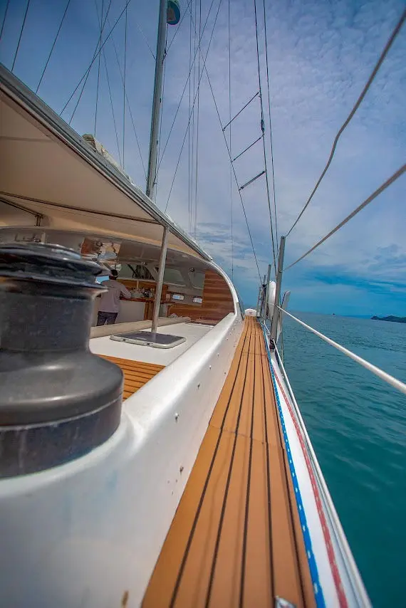 Teak side deck, winch and rigging along the hull of a sailing catamaran under a blue sky