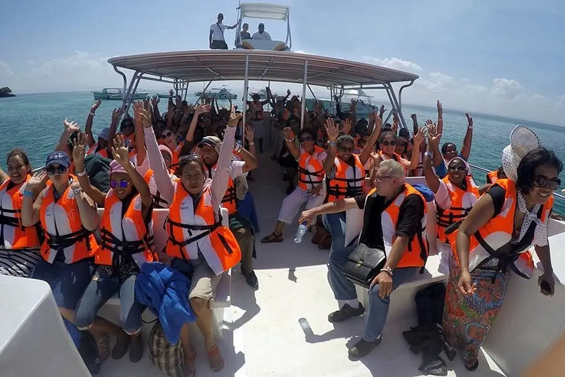 Whale watchers in orange life jackets cheering with raised arms under a power catamaran's canopy