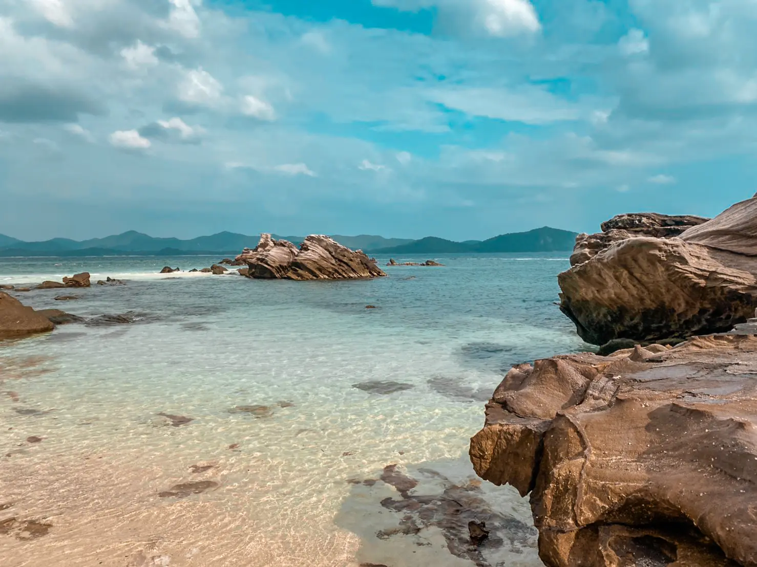 Rounded boulders in clear shallow water with distant mountains on the horizon off the Khai islands