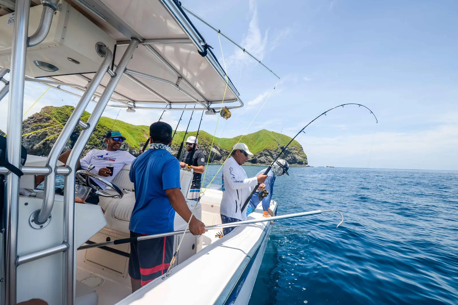 Anglers on a center console boat fighting a fish on a bent rod near green Papagayo headlands