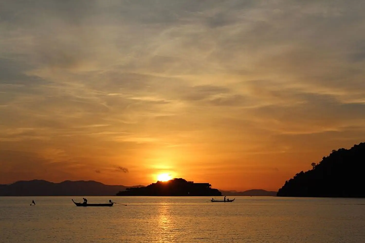 Two small boats silhouetted on a calm sea under an orange sunset sky in Thailand