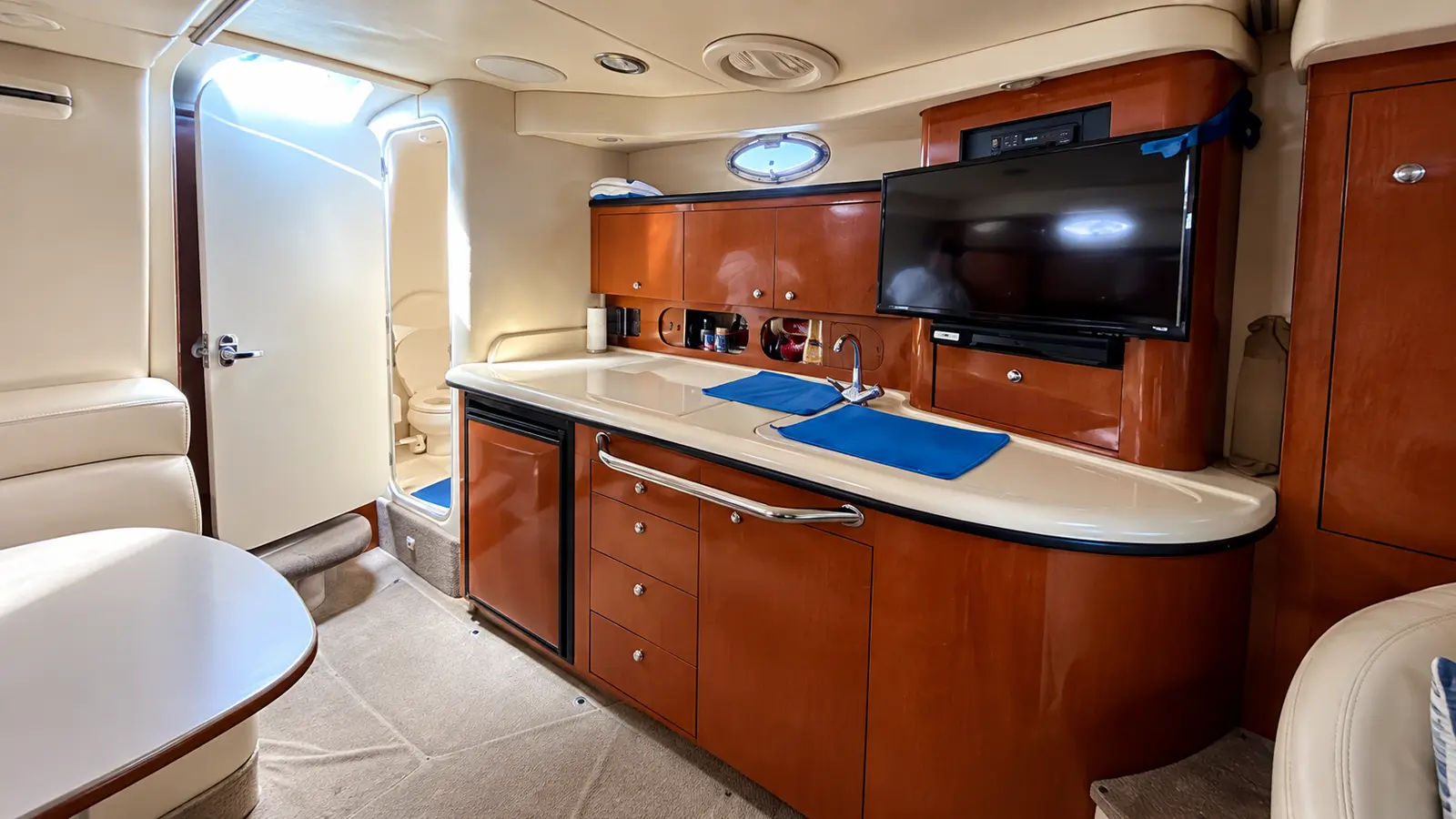 Cabin galley with cherry wood cabinets, cream counter and flat-screen TV inside a motor yacht