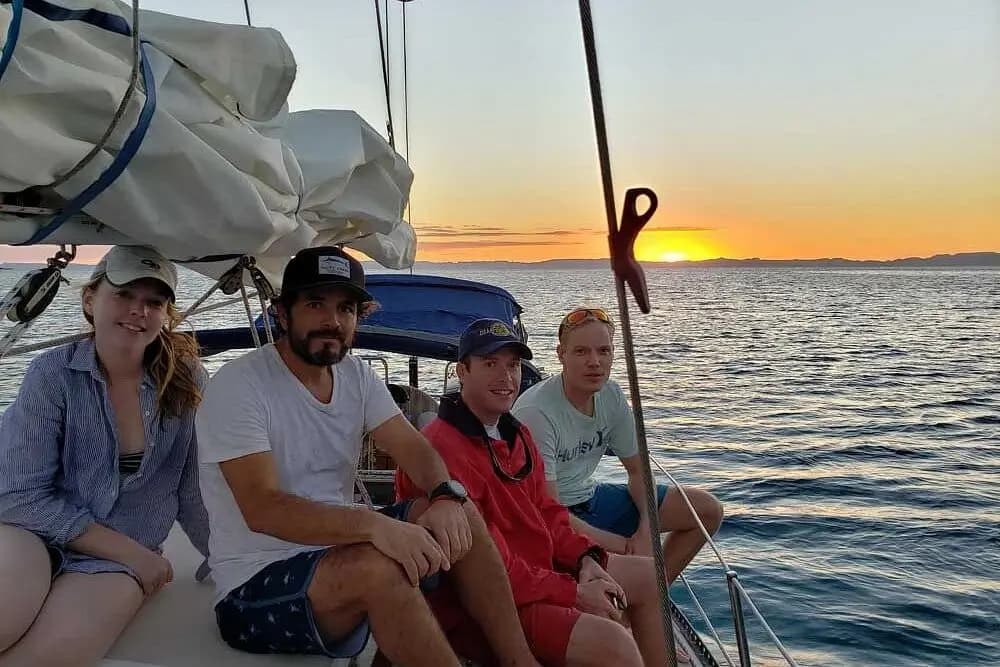 Four guests sit on the sailboat's deck as the sun sets over the Sea of Cortez