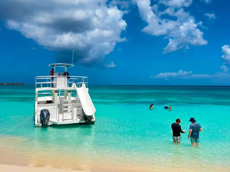 Two-deck catamaran with a water slide anchored in the turquoise shallows of Bahía de las Águilas