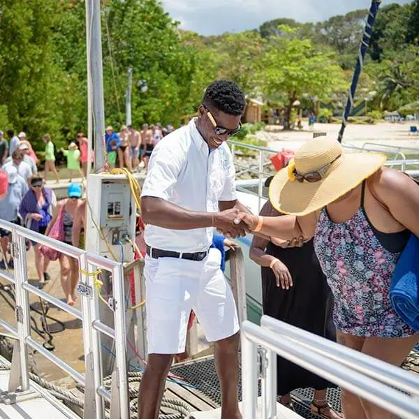 A crew member in white helping a woman in a sun hat board the catamaran at an Ocho Rios dock