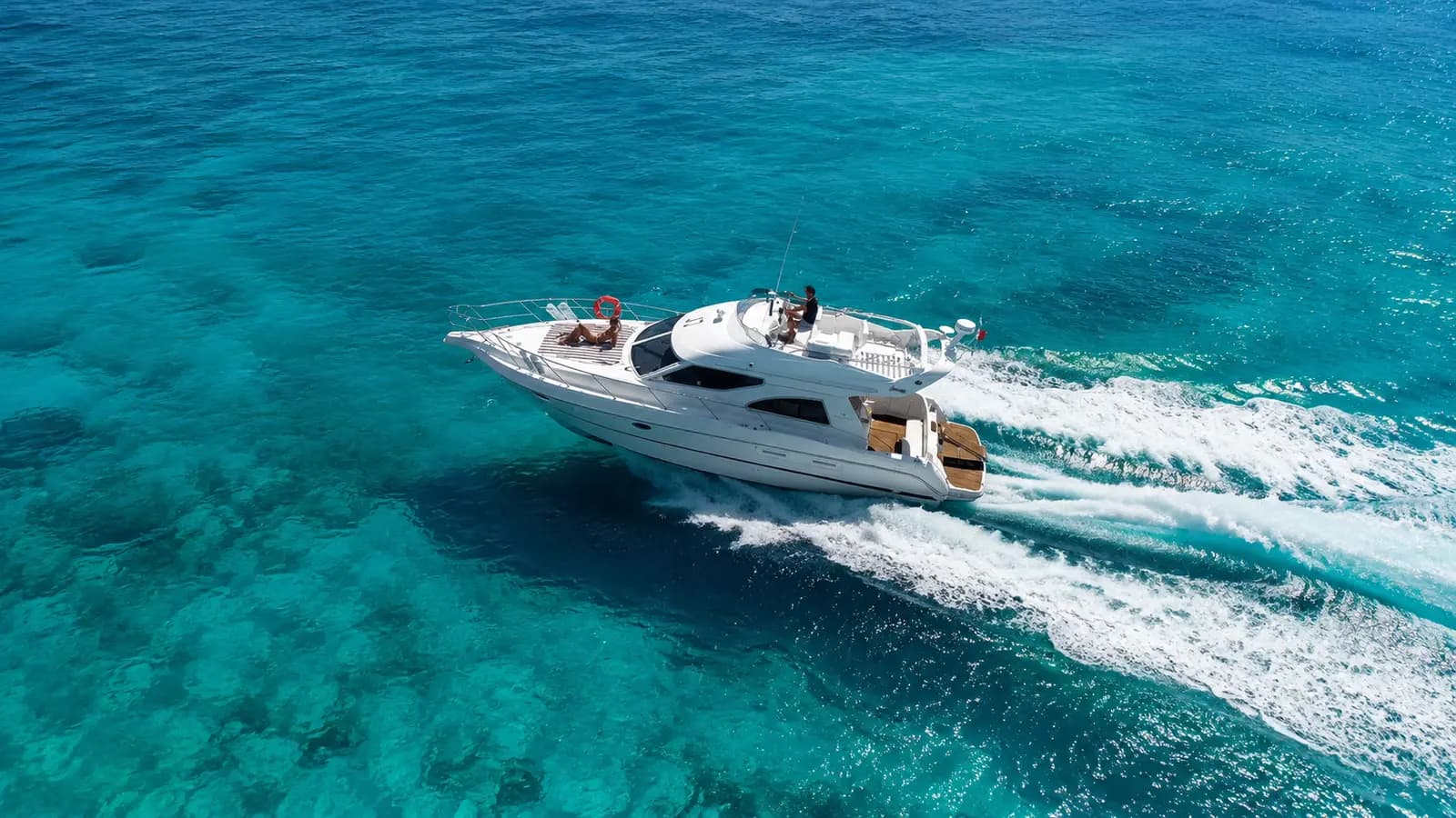 Aerial view of a flybridge motor yacht speeding across turquoise water off Mykonos, trailing a white wake