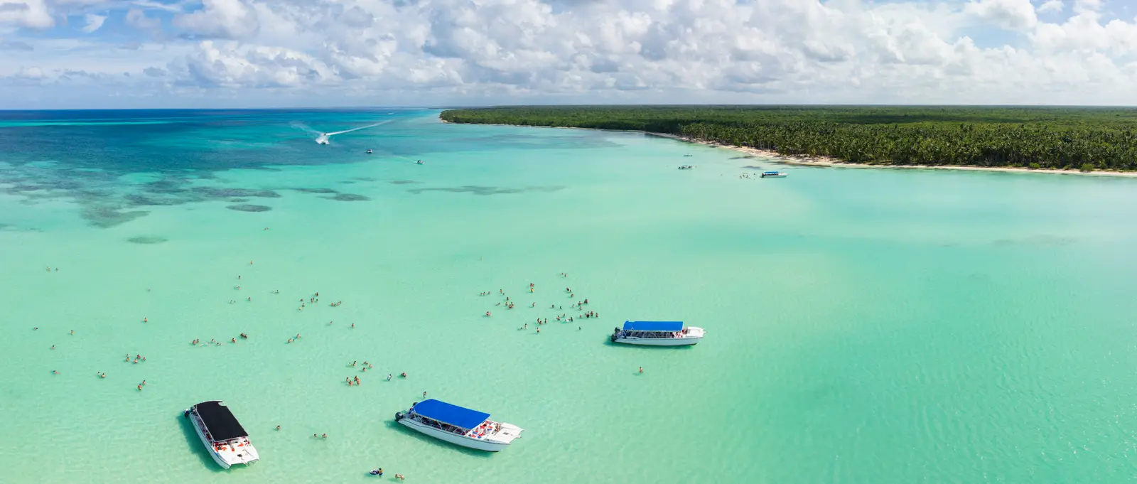 Speedboats with blue canopies anchored amid crowds of swimmers in the Saona Island natural pool