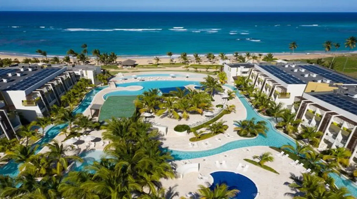 Aerial view of a Punta Cana beach resort with winding pools, palm gardens and solar-paneled buildings