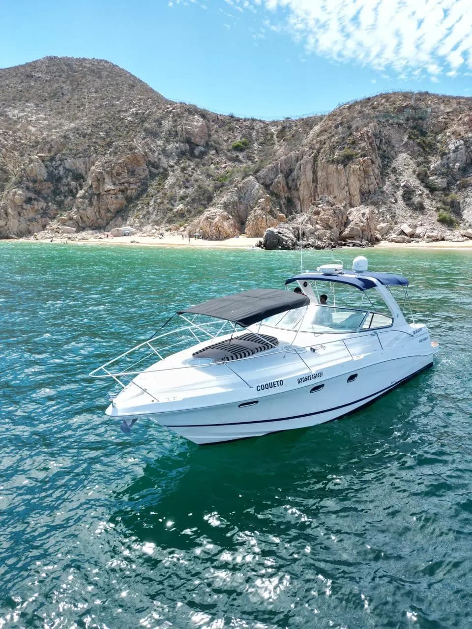 Aerial view of the yacht floating off a rugged granite hillside and small beach in Los Cabos
