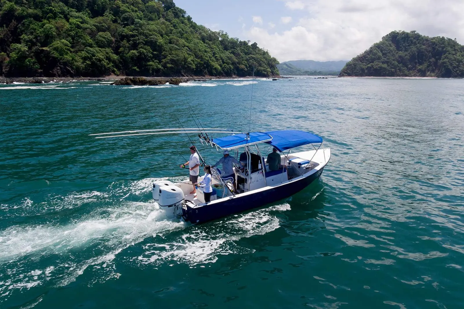 Center-console fishing boat with a blue T-top running between forested headlands off Costa Rica