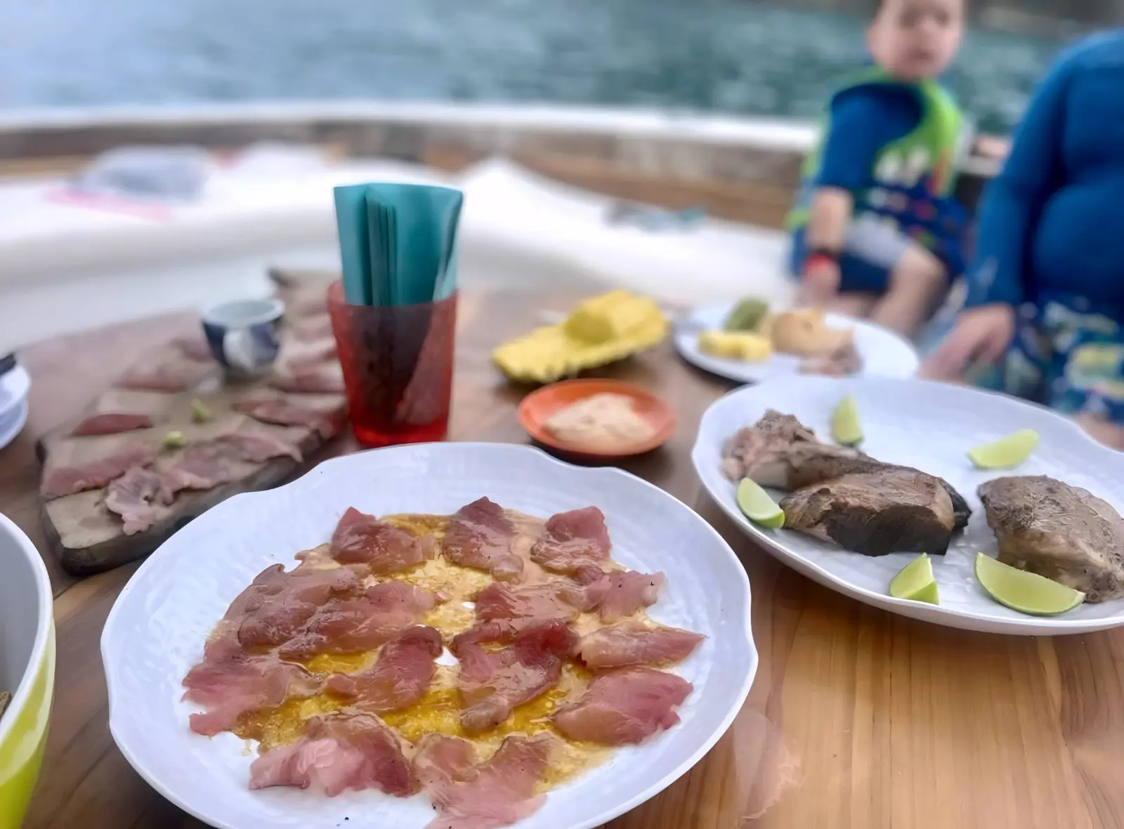 Plates of tuna sashimi and seared tuna steaks with lime on the boat's table, a child nearby
