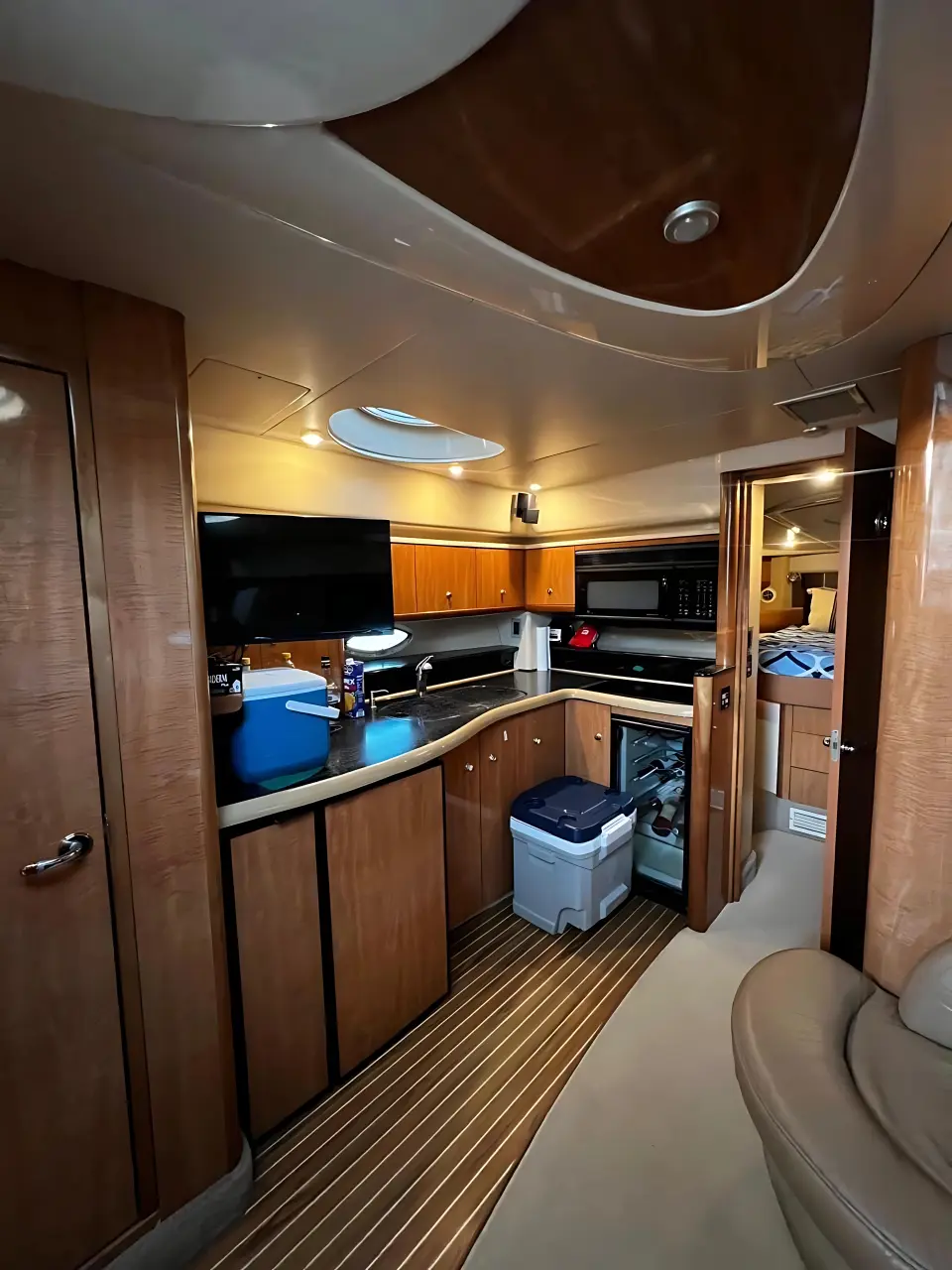 Yacht cabin with glossy wood cabinets, a galley counter, a cooler and striped teak flooring