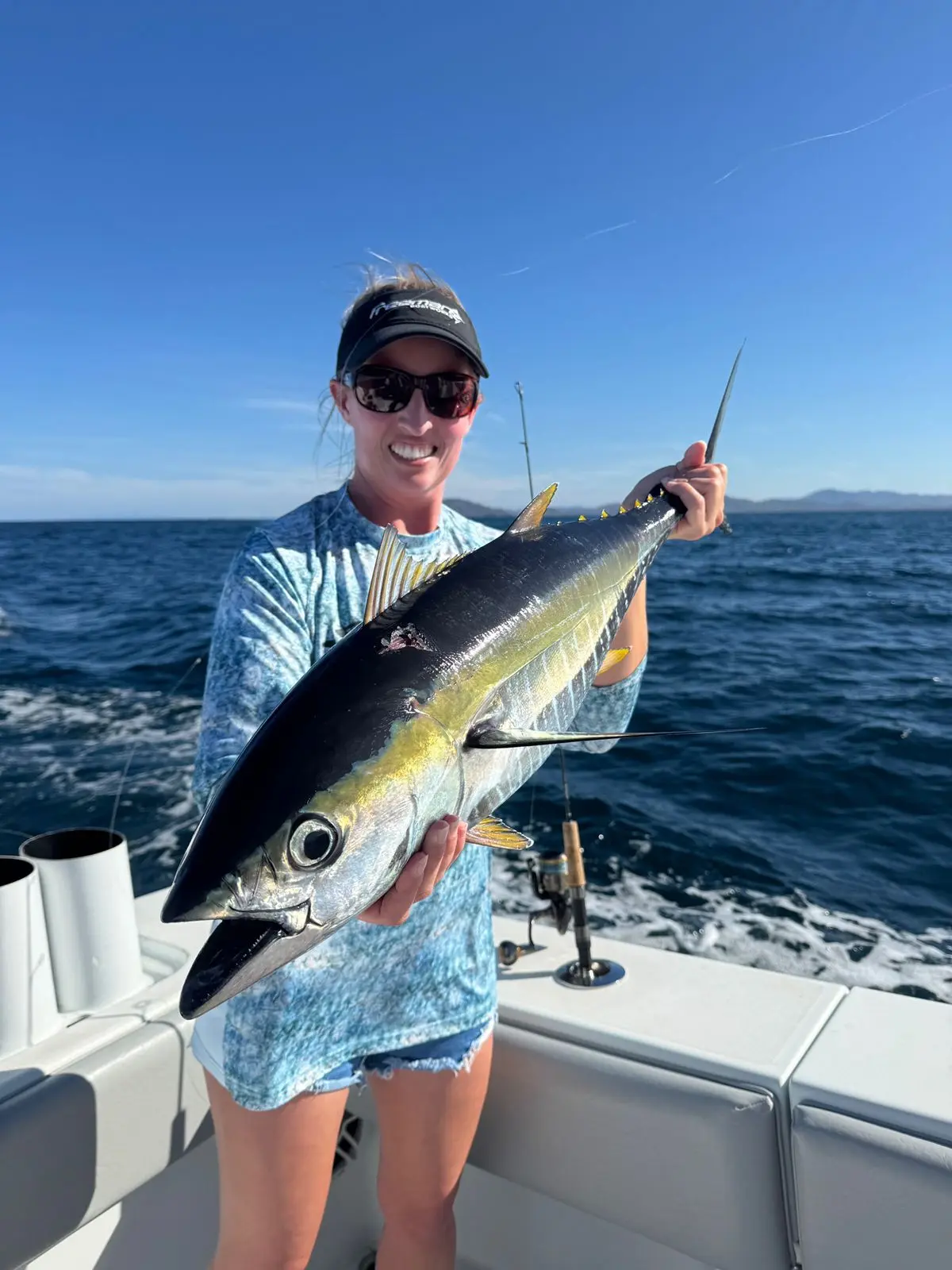 Woman in a cap and sunglasses holding a yellowfin tuna on the deck of a sportfishing boat