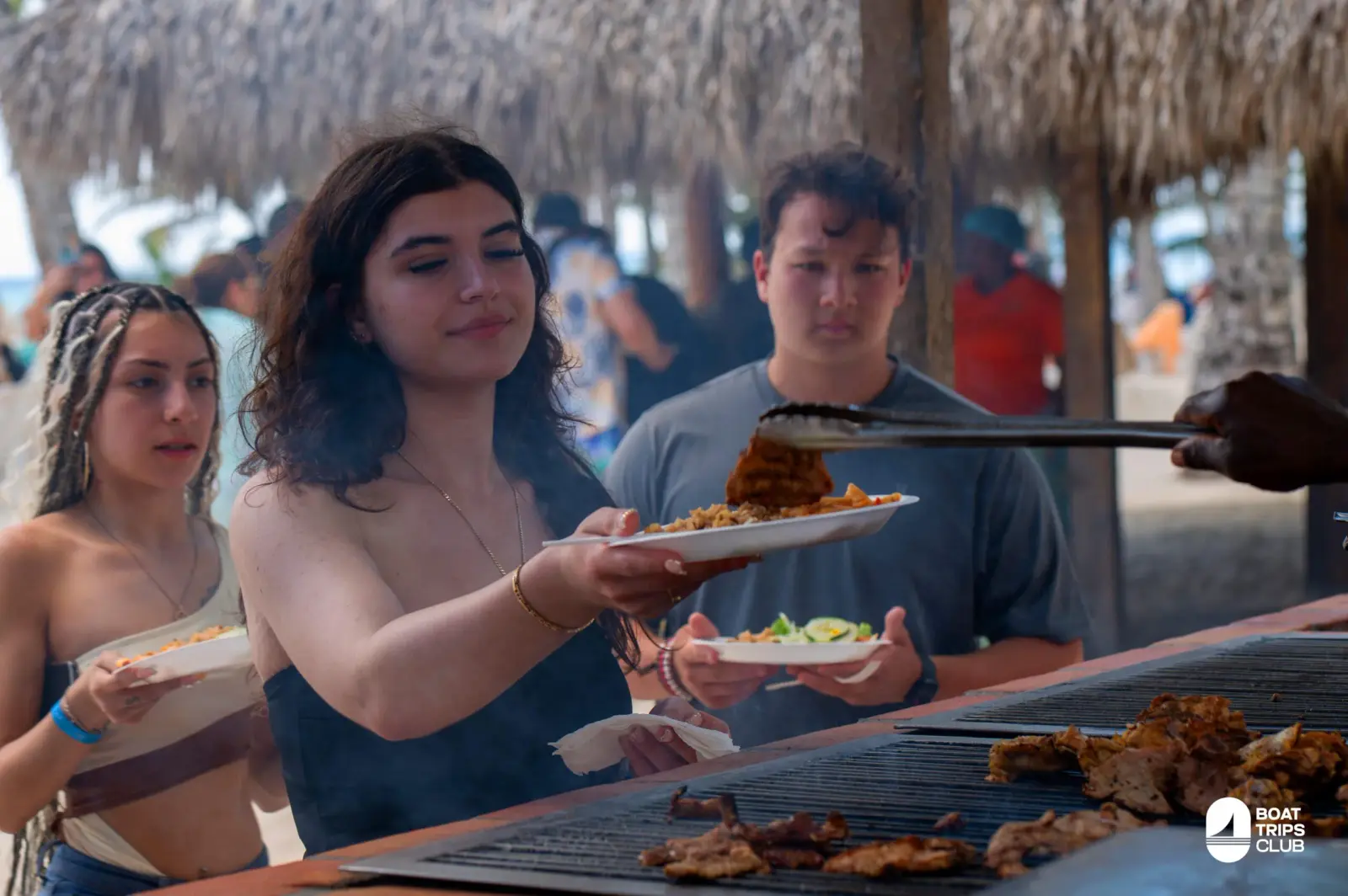 Guests holding plates as grilled chicken is served at a buffet under a thatched roof on Saona Island