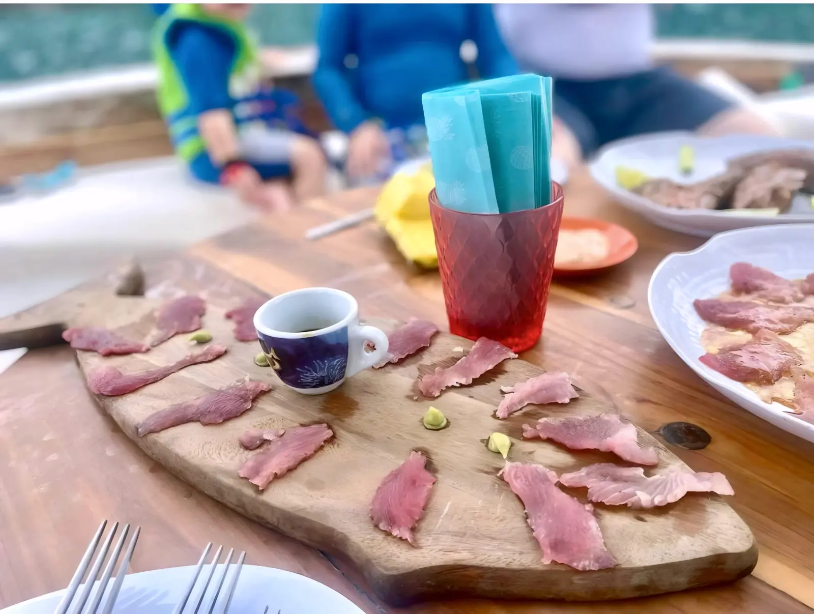 Slices of fresh tuna on a wooden board with a small cup of soy sauce on the deck table