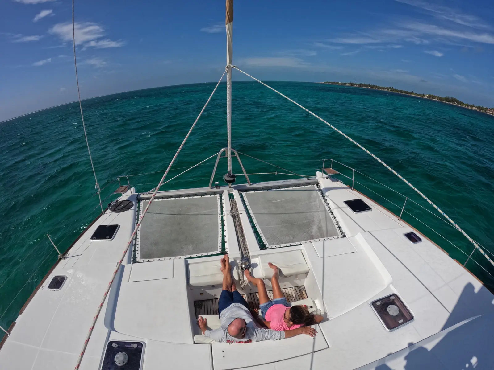 View from the mast of a couple lounging on the foredeck of a sailing catamaran off Belize