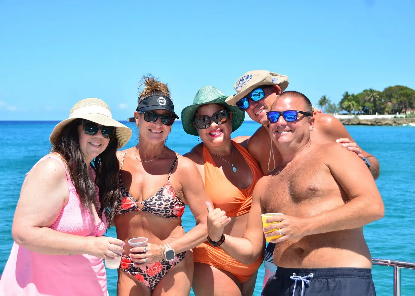 Five guests in hats and sunglasses posing with drinks at the catamaran rail off Puerto Plata