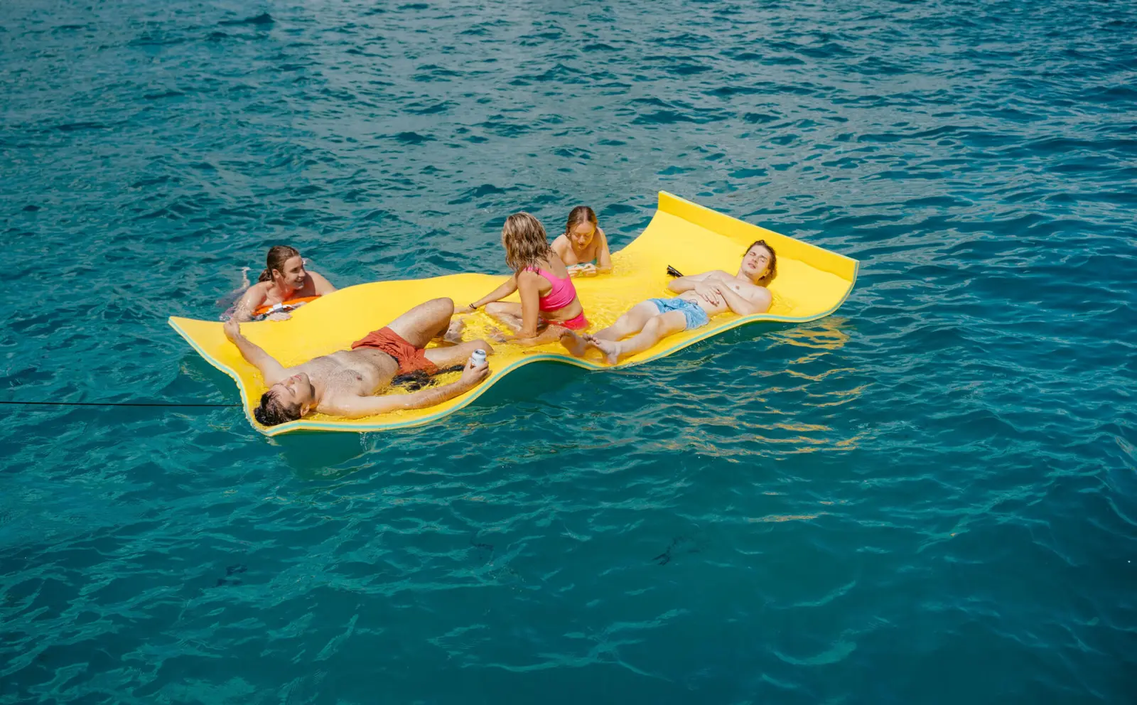 Guests stretched out on a yellow foam water mat floating on deep blue sea