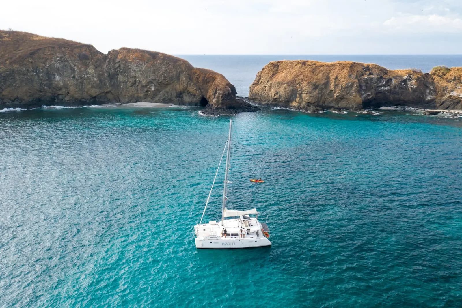 Drone view of a sailing catamaran anchored in a clear turquoise cove ringed by rocky islets in Costa Rica