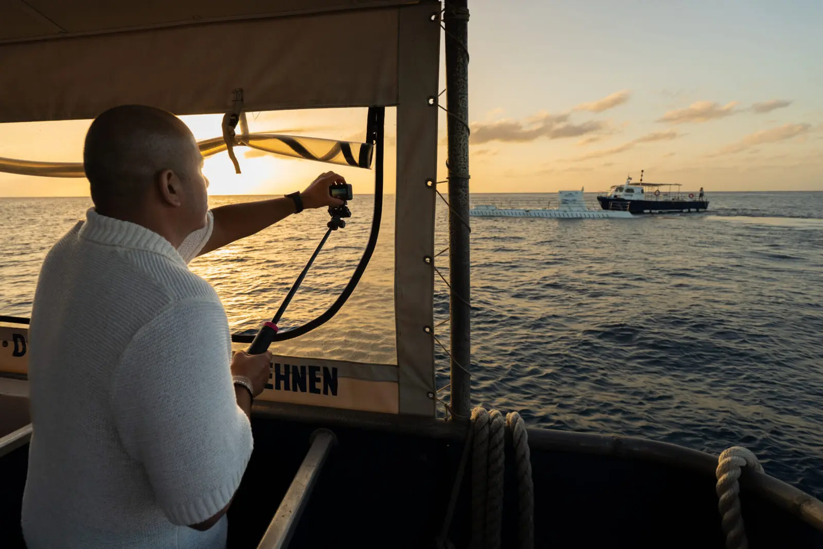 Guest filming the sea from a covered boat deck in golden light as another vessel passes off Cozumel