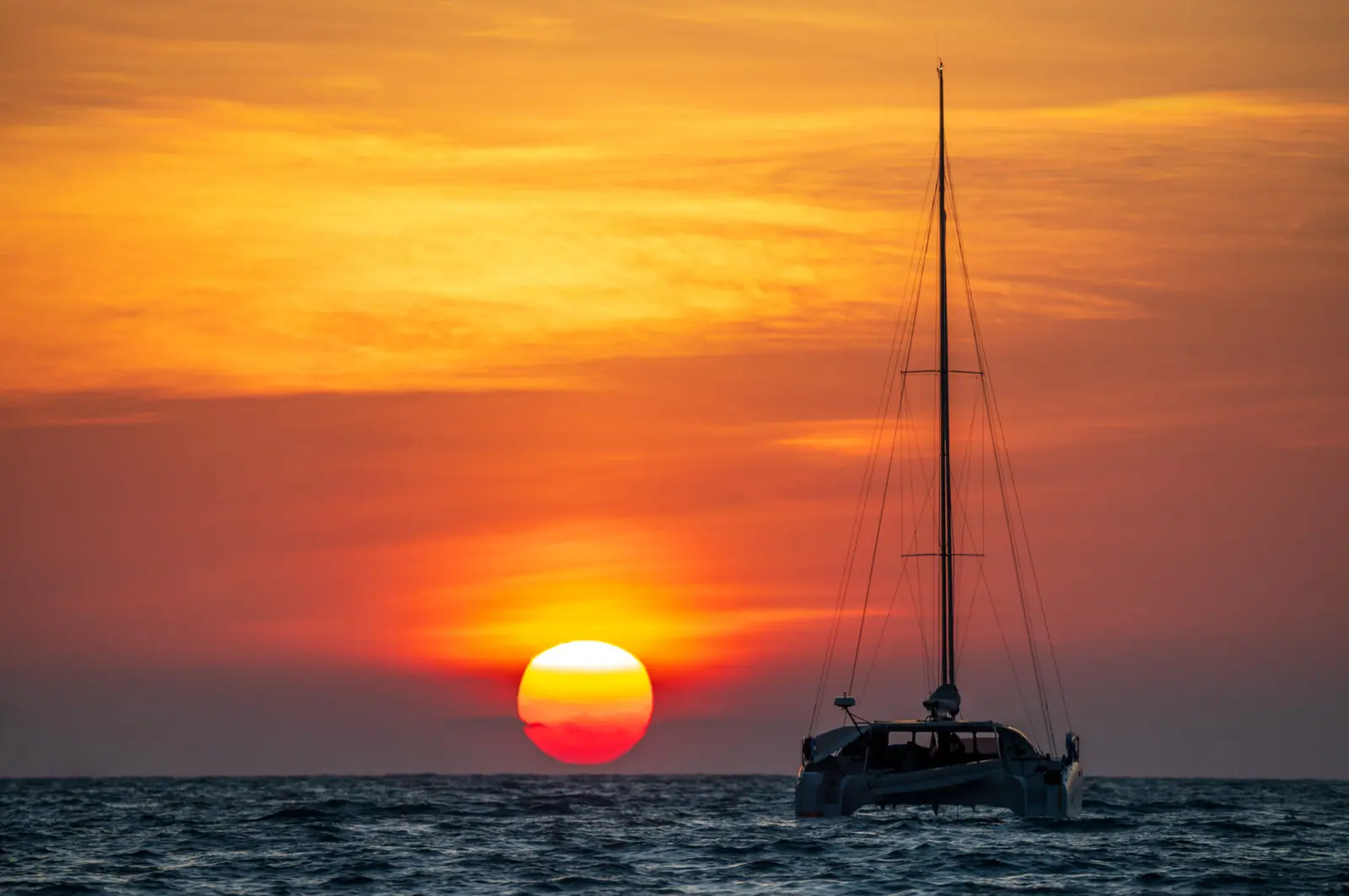 Sailing catamaran silhouetted on the sea as an orange sun sets on the horizon near Cancún