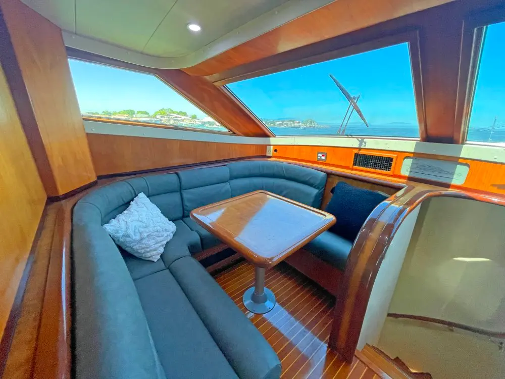 Blue-gray U-shaped settee around a varnished table under wide yacht windows looking out to the water