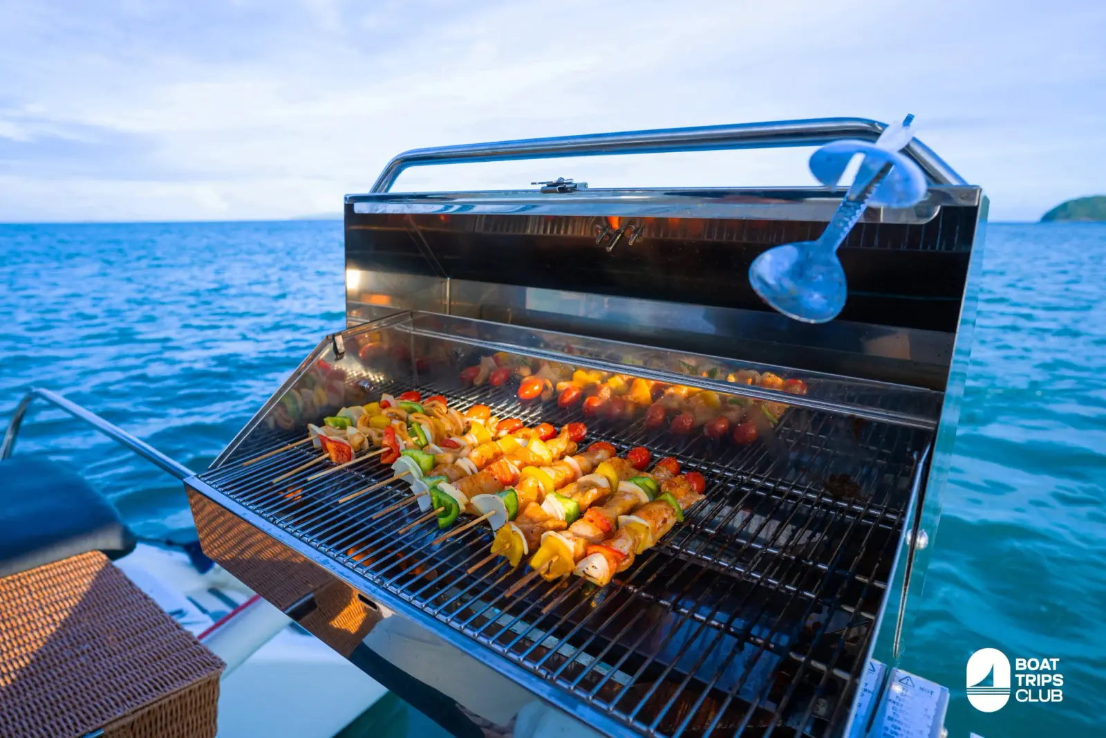 Colorful kebabs grilling on a stainless BBQ on the catamaran deck, blue sea and an island behind