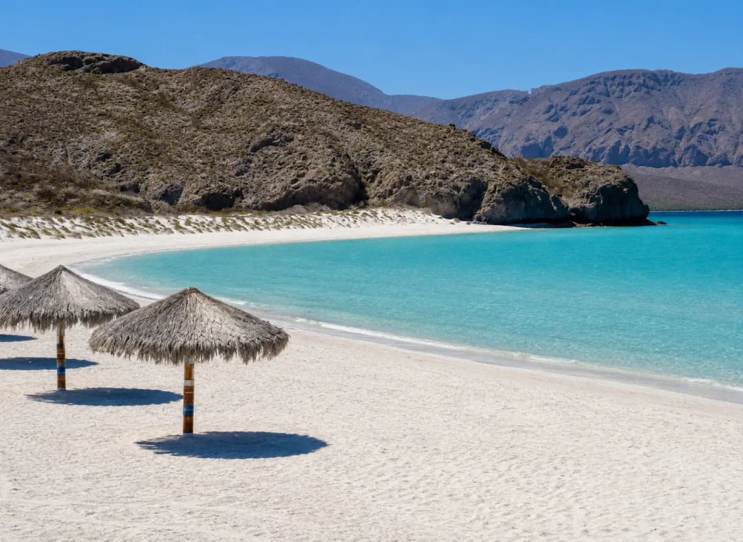 Balandra Beach with white sand, turquoise water, thatched umbrellas, and rugged desert mountains in Baja California Sur