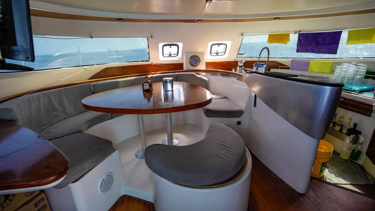 Catamaran saloon with a round wooden table, curved grey bench seating and a galley counter