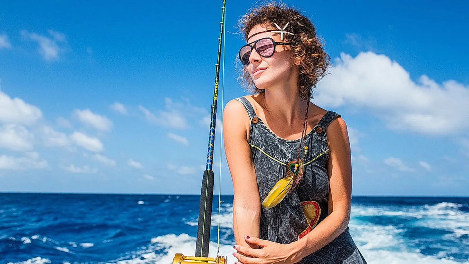 Woman posing beside a trolling rod at the stern above the boat's foamy wake