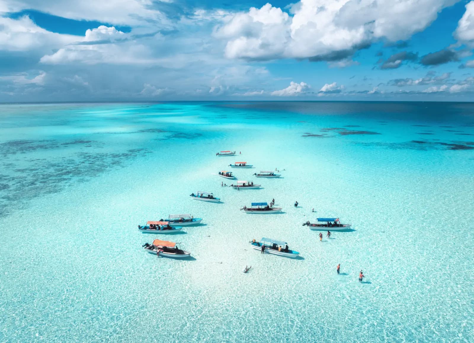 Bird's-eye view of small boats anchored over pale turquoise shallows with swimmers nearby off Zanzibar