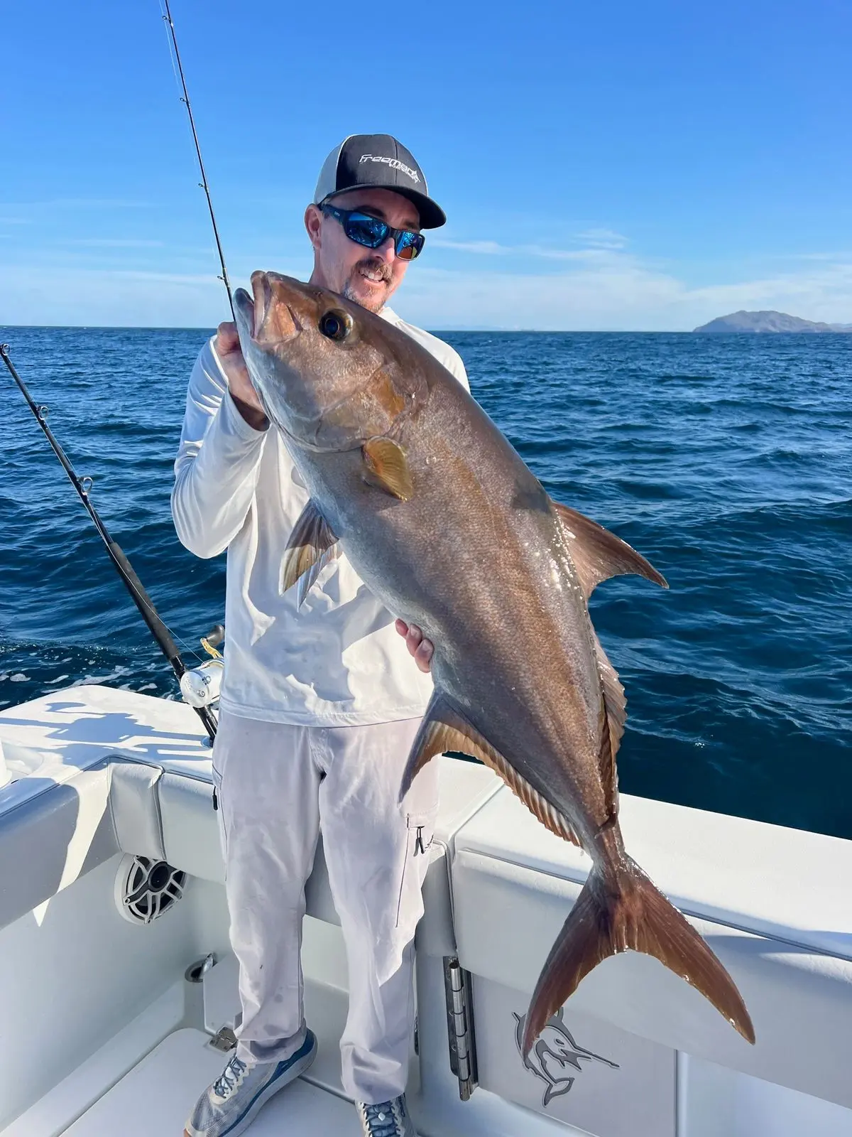 An angler in a cap and sunglasses holds up a large gray fish at the stern of the sportfishing boat