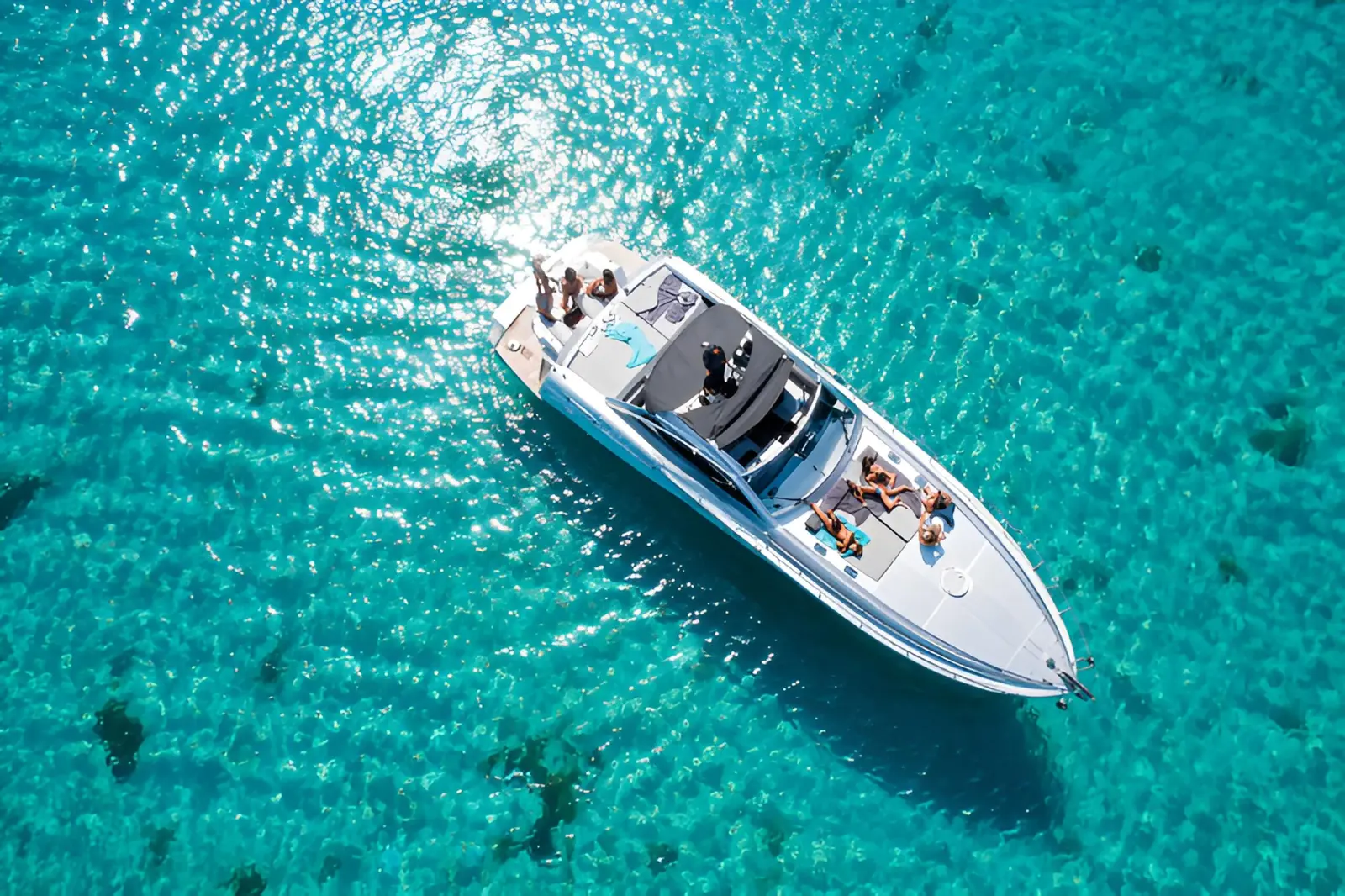 Aerial view of a white sport yacht anchored in clear turquoise water off Mykonos, guests lounging on deck