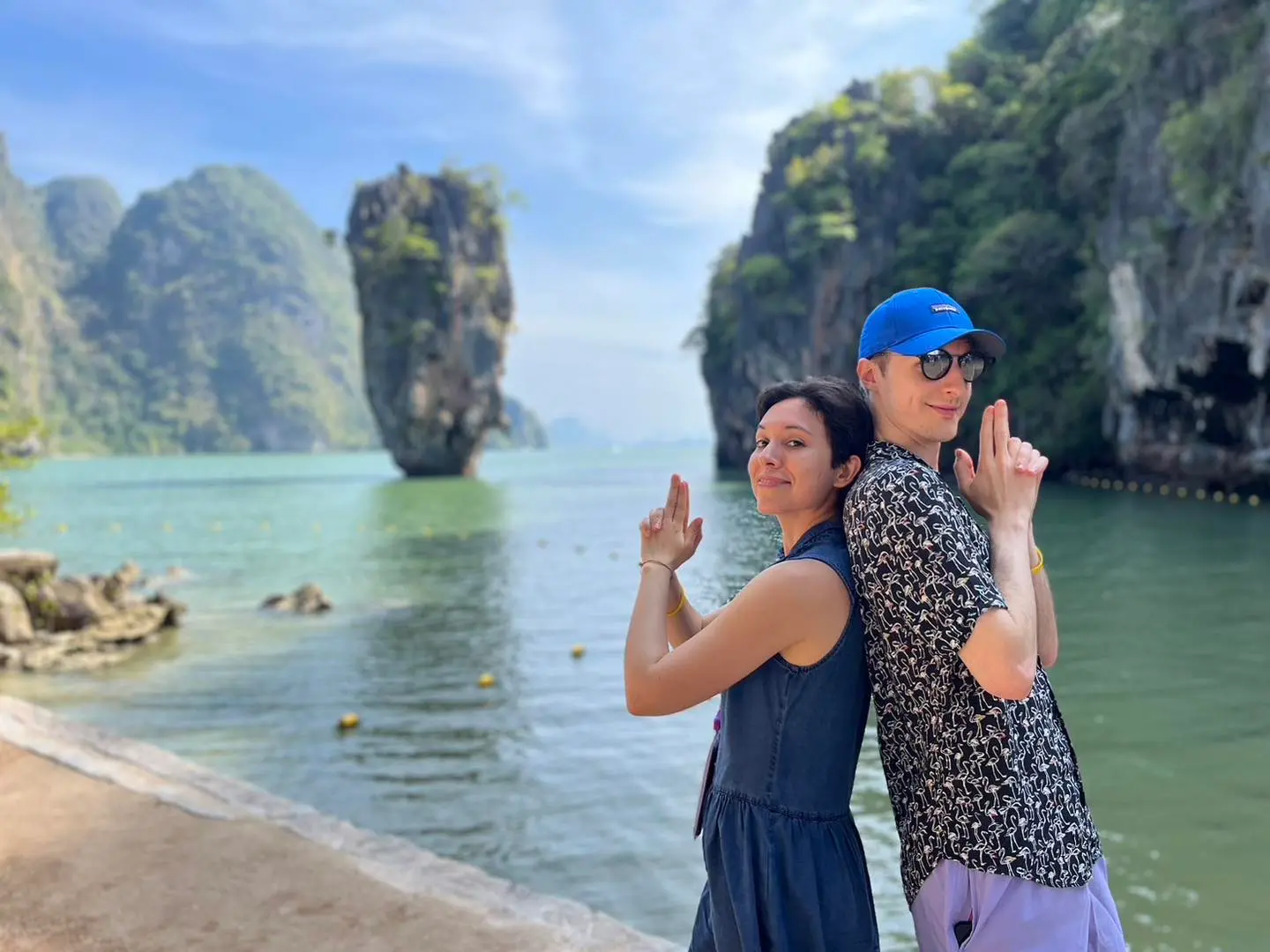 Couple standing back to back in finger-gun poses, the James Bond Island sea stack behind them
