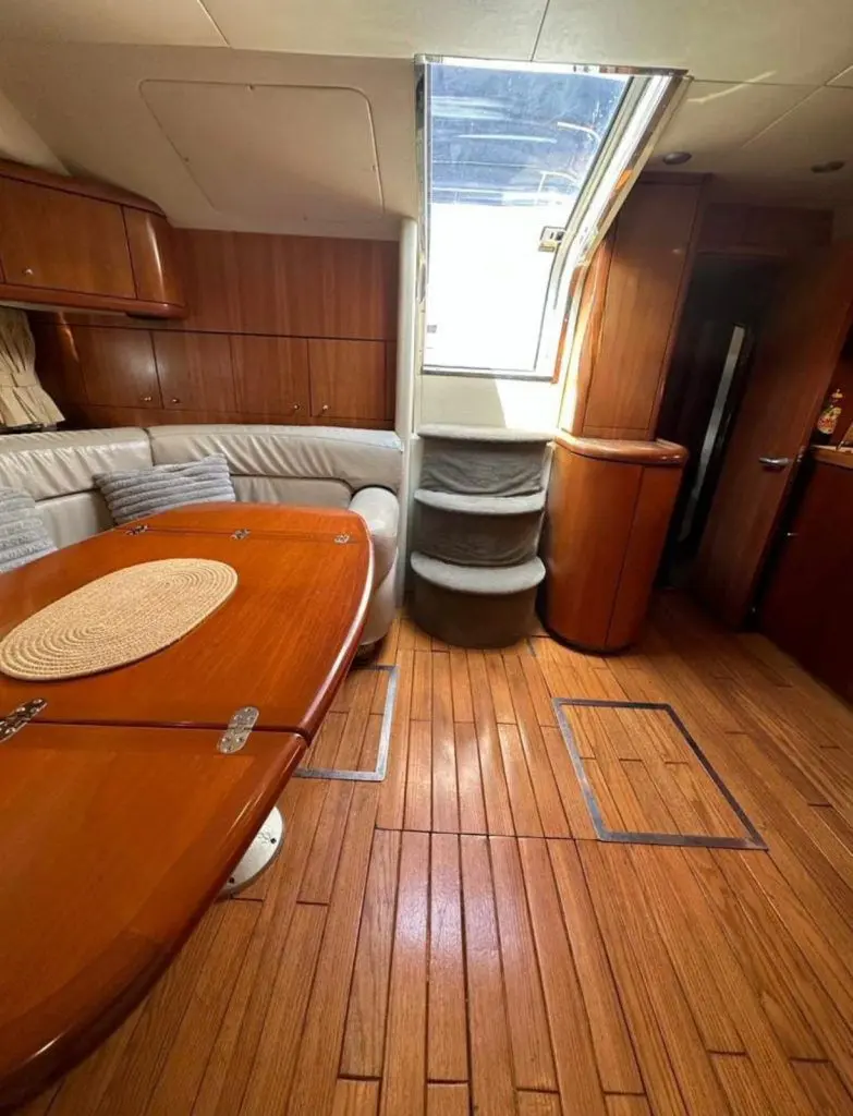 Wood-paneled salon of the yacht with a long table, curved sofa and teak floor