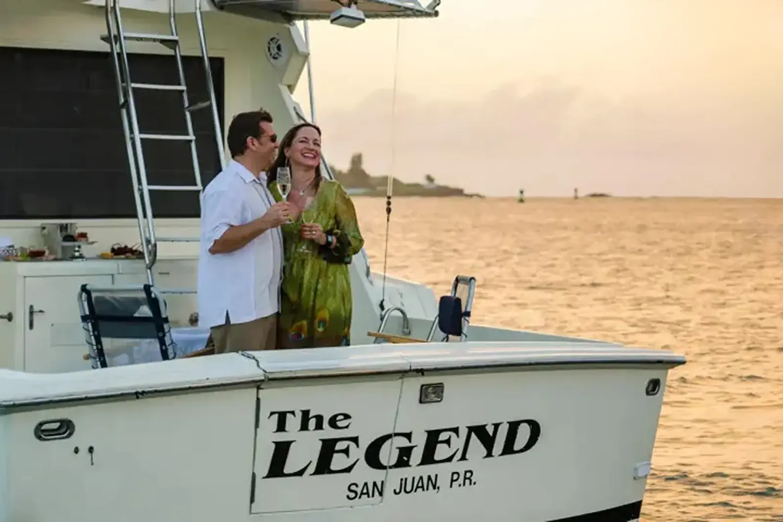 Couple with drinks on the aft deck of a powerboat as the sun sets over San Juan Bay
